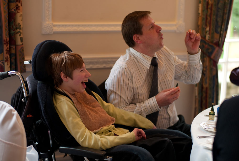 A father blowing bubbles to entertain his disabled son at the wedding breakfast