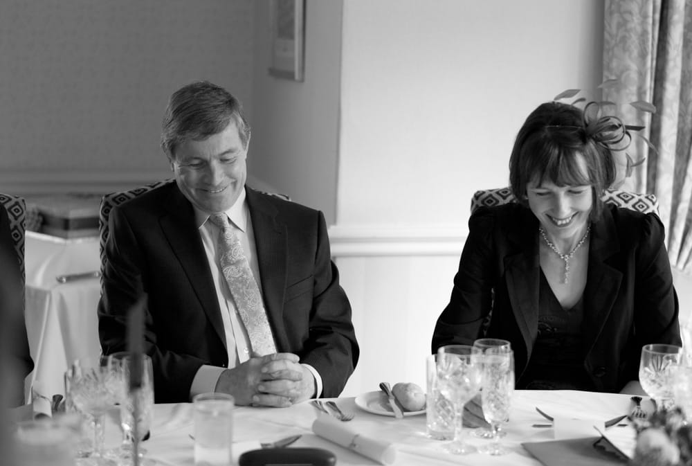 Groom’s parents looking down, smiling warmly at Weetwood Hall wedding breakfast.