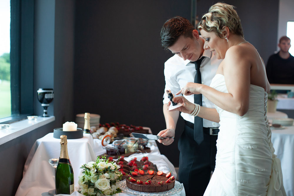 The couple smile as they look closely at their unique cake topper.