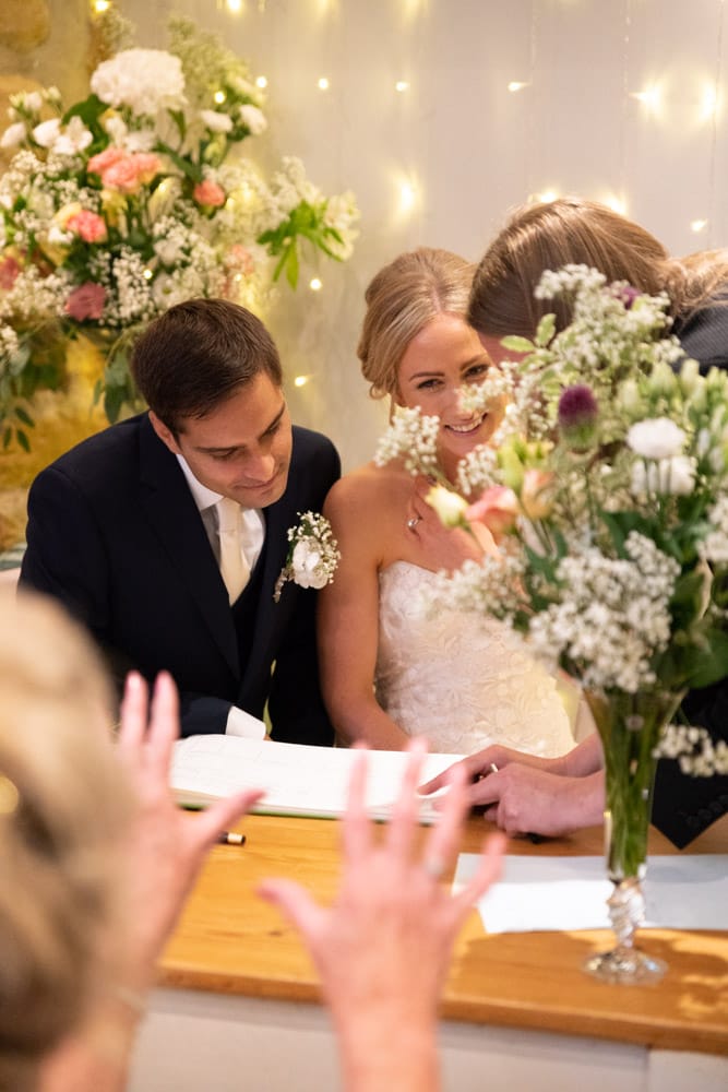Registrar gestures to the register as Helen smiles warmly at her mum through flowers on the table.