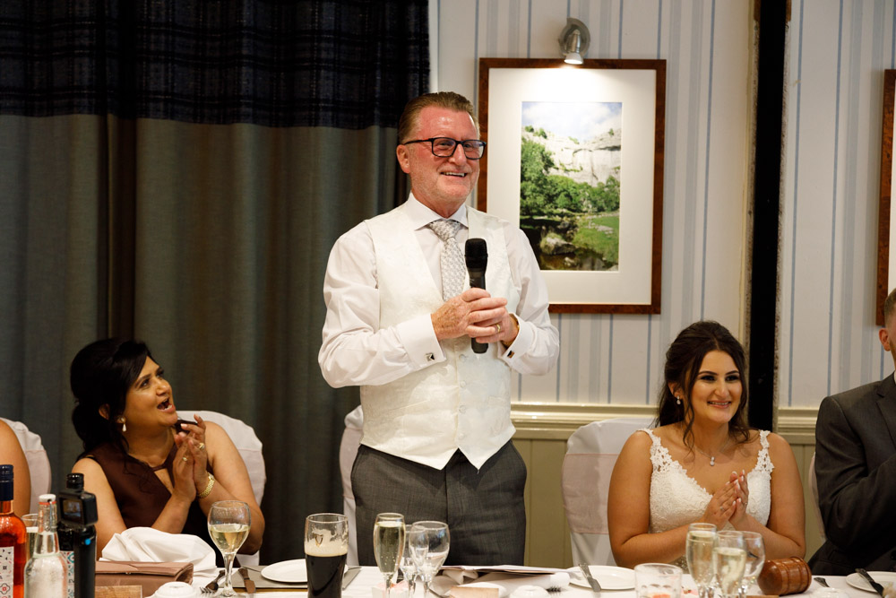 The father of the bride begins his speech, met with smiles and applause.