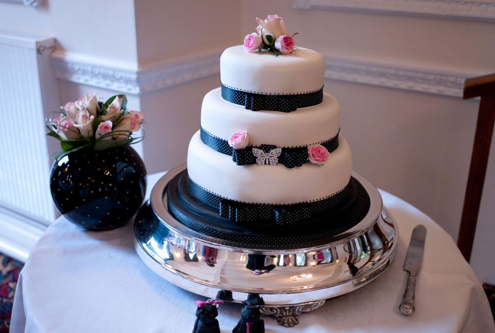 Three-tier white wedding cake with black ribbon and white rose detail