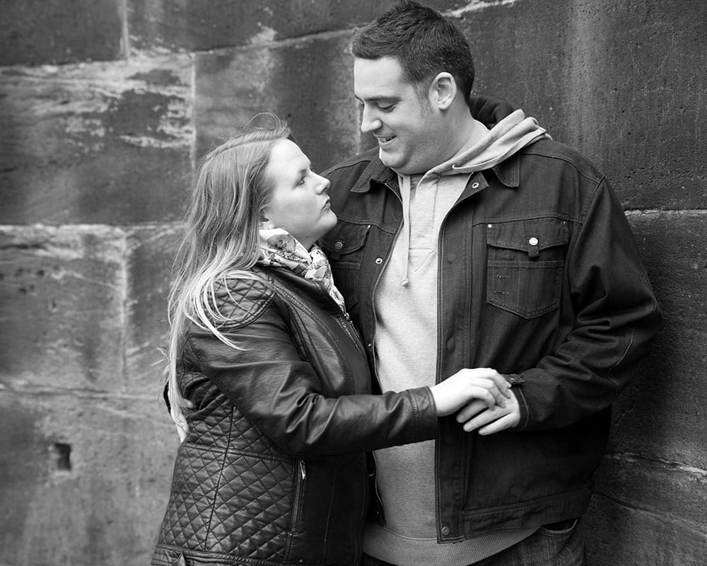 Black and white photo of Lisa and Oliver standing by the Abbey wall, gazing at each other.