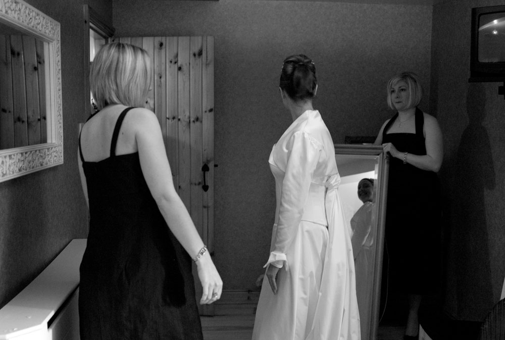The bride looks into a mirror held by her sister.