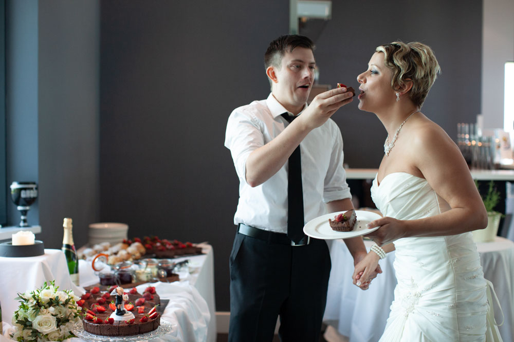 Tim feeds Sam a bite of cheesecake as she smiles, enjoying the playful moment.