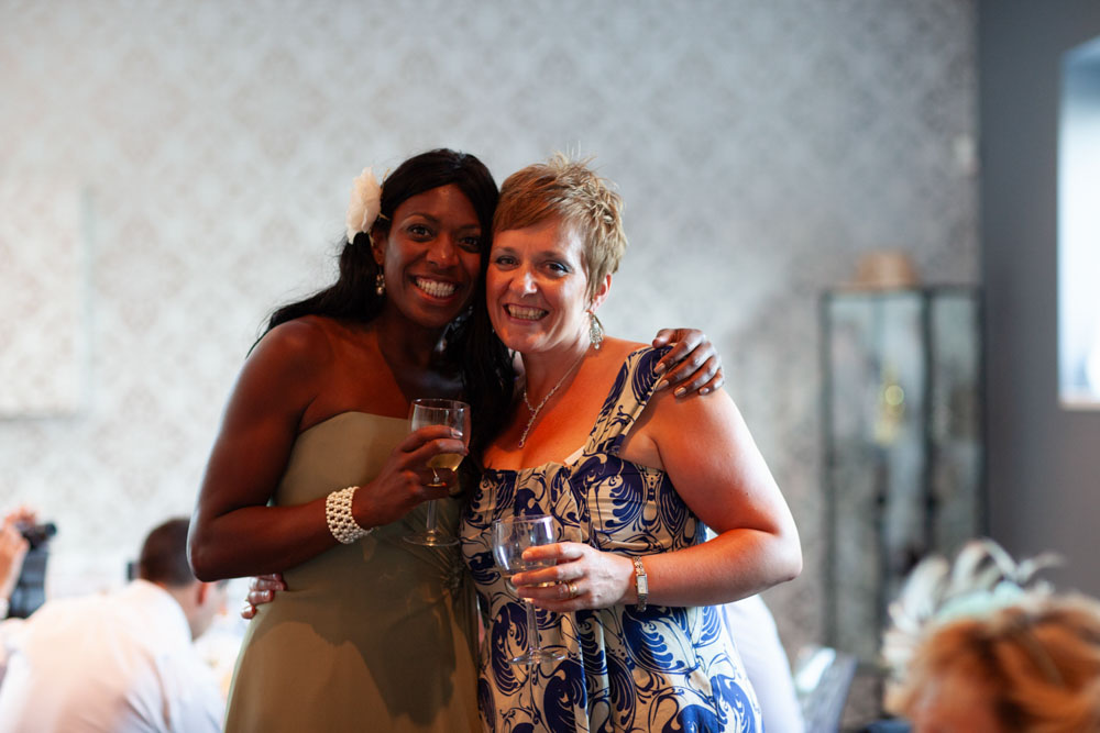 A bridesmaid stands smiling beside her friend, both posing happily for a photo.