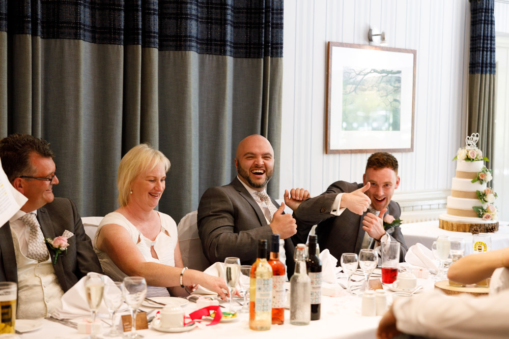 One best man smiles and gives a thumbs-up to the photographer mid-speech.