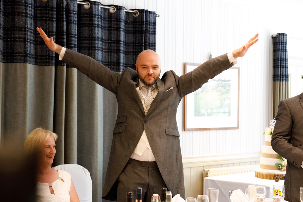 The first best man opens his speech with arms wide and energy, full of personality.