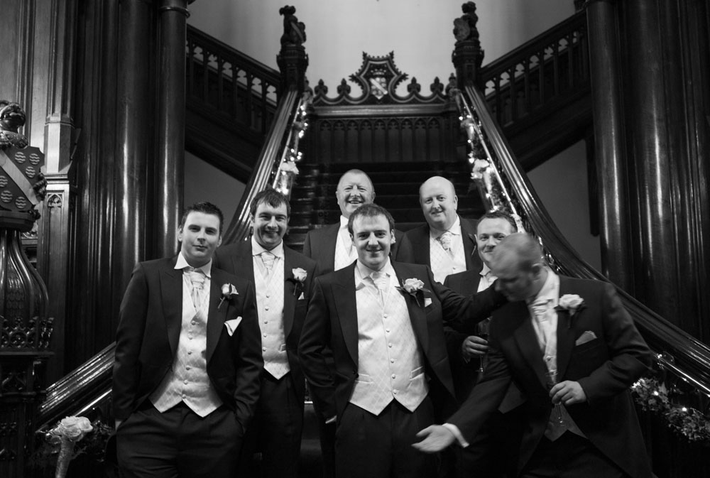 Groomsmen on the grand staircase of Allerton Castle, one joking with the groom