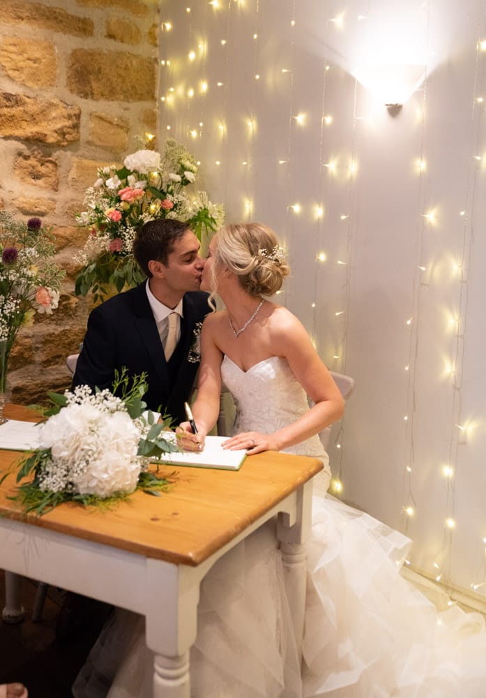 The couple share a kiss by the signing table, bouquet nearby.
