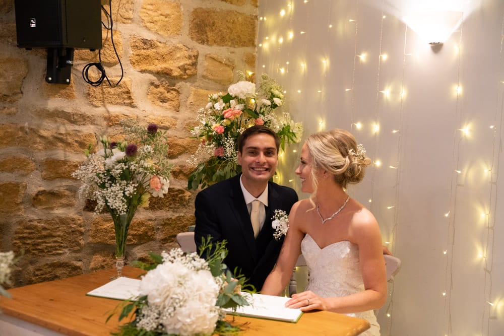 Adam beams with a wide smile as Helen looks at him laughing in response.