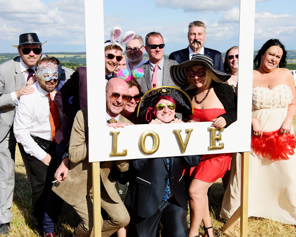 Larger group poses around the photo frame outside the tent in celebration.