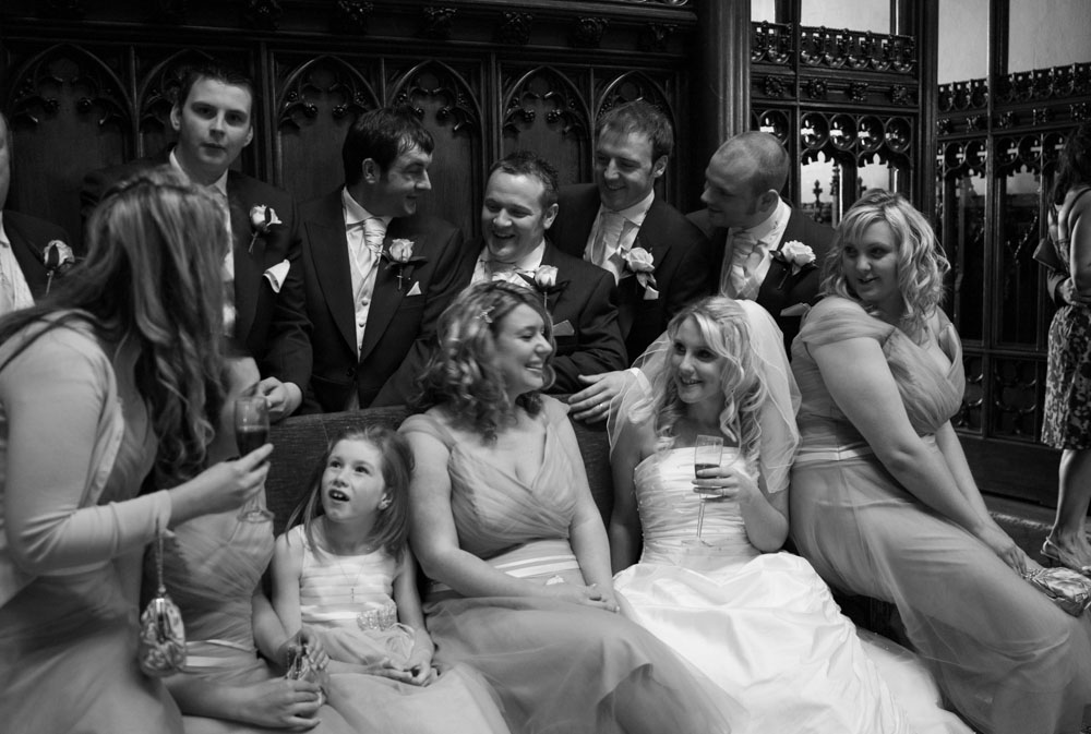 Bridesmaids seated with groomsmen standing behind, captured in black and white