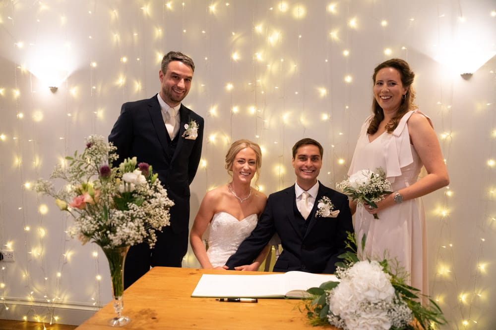 The couple sit while witnesses stand posed behind with fairy lights glowing.