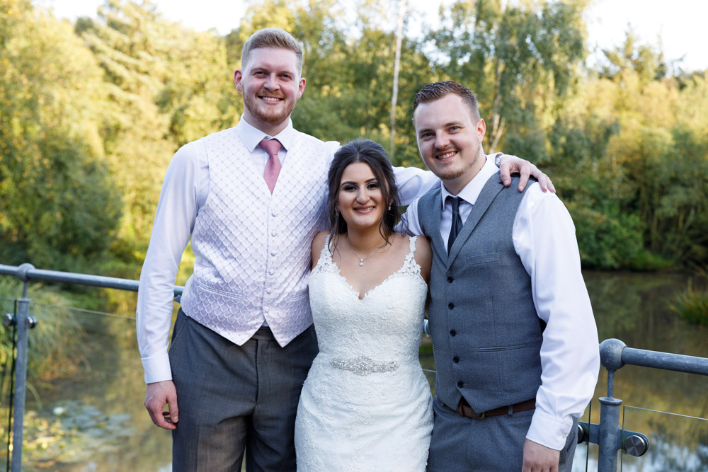 Kyra stands centre with Matt and a friend, trees and water behind them at Chevin Lodge.