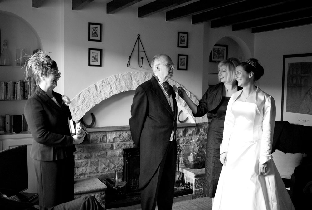 The bride, her sister, and parents gather smiling downstairs.