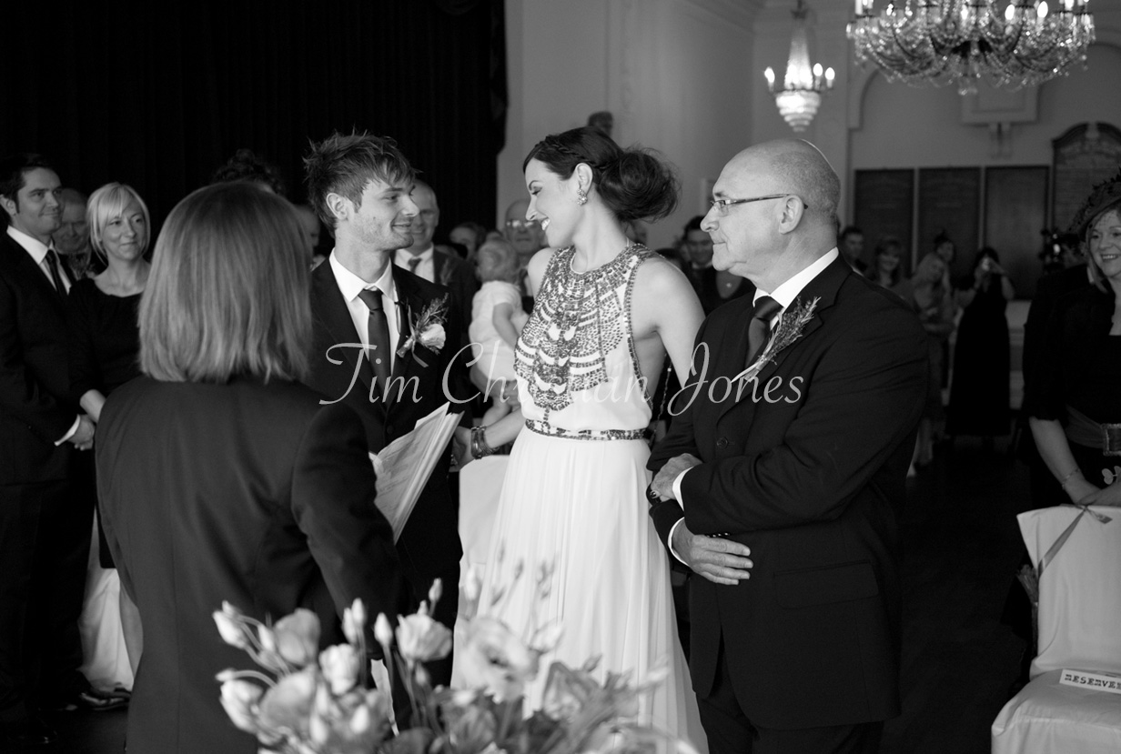 The bride arrives smiling, her father proudly walking her down the aisle toward the groom.
