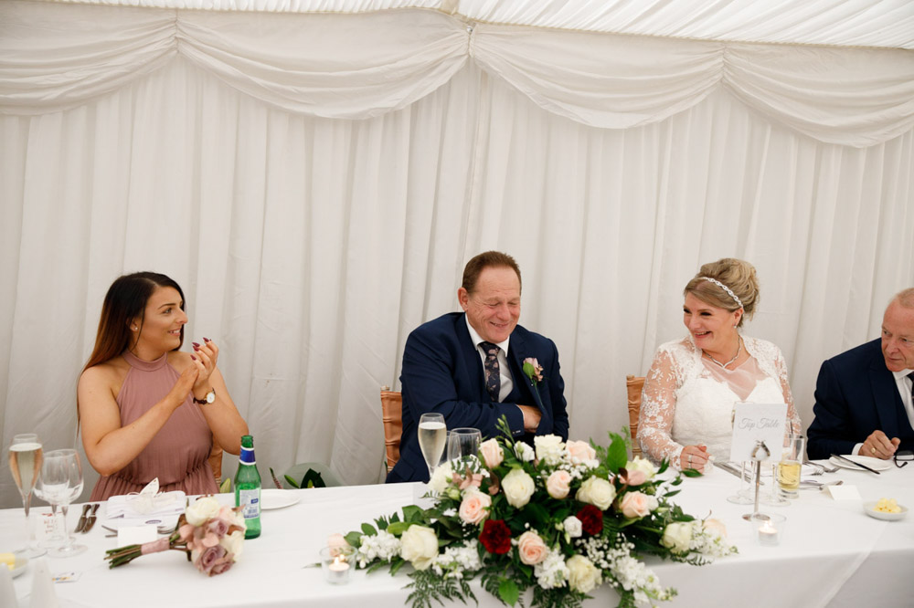 The couple seated at the top table, smiling during applause before speeches.