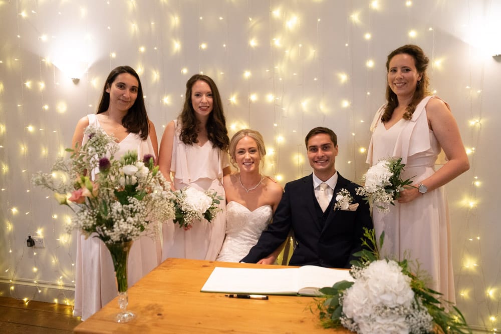 The couple sit with three bridesmaids, two on one side and one on the other, all smiling.