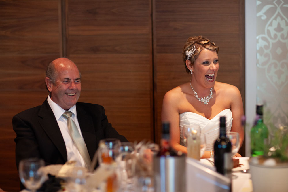 Sam sits beside her father, both smiling in a quiet, heartfelt moment.