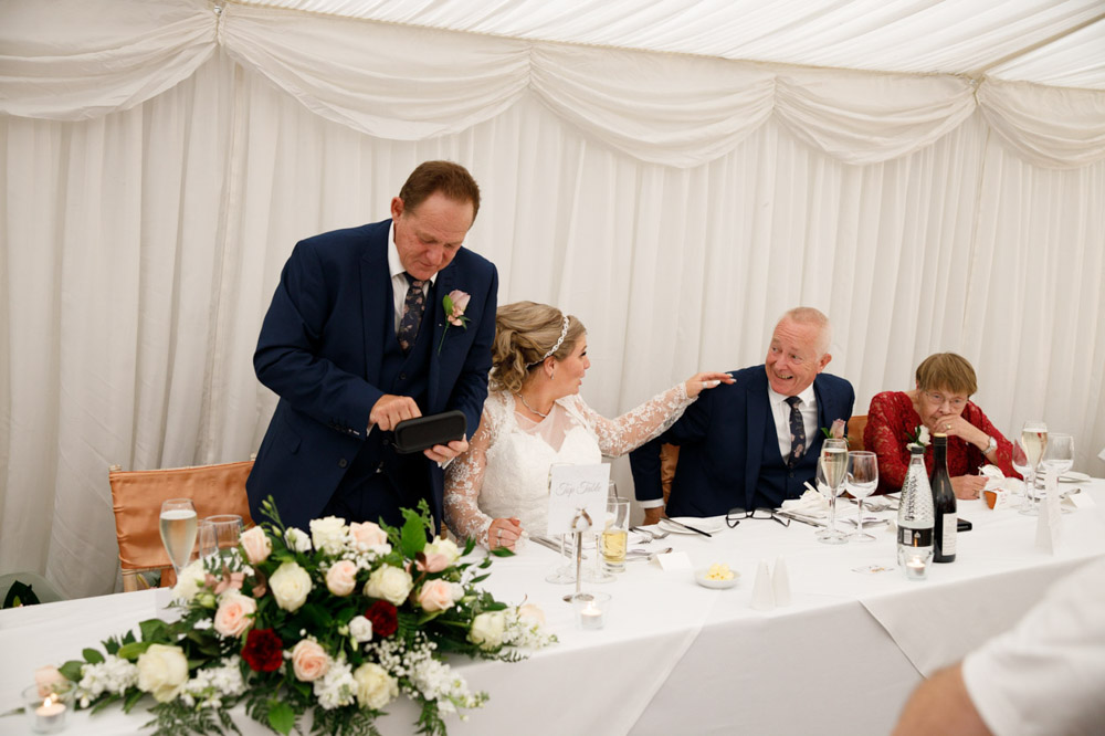 Gary begins his speech while Tracy looks at her father, her hand resting gently on his shoulder.