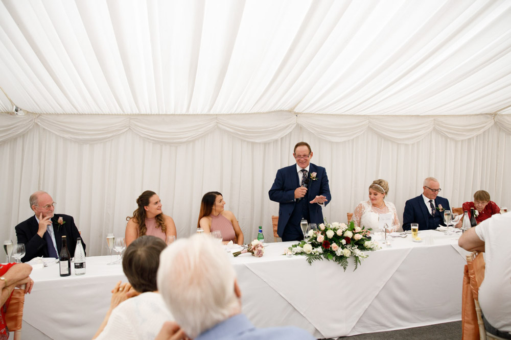 A wide shot of Gary giving his speech, guests listening intently across the room.