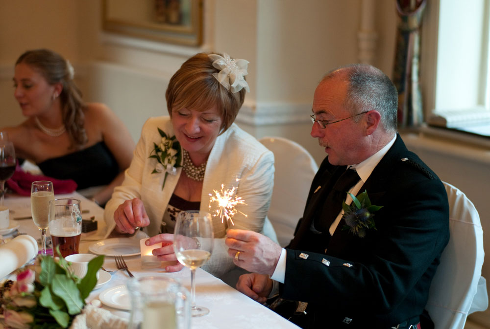 Dani’s father holds a sparkler at the top table while his wife smiles beside him.