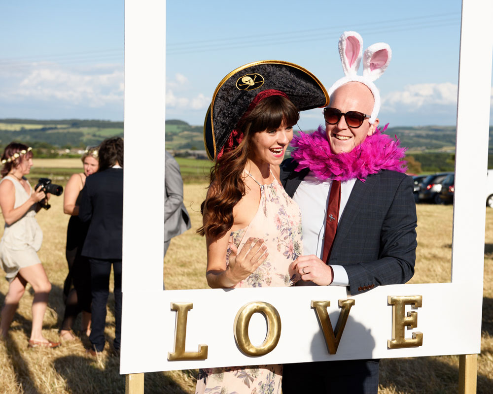 More wedding guests pose and laugh at the love photo frame outside.