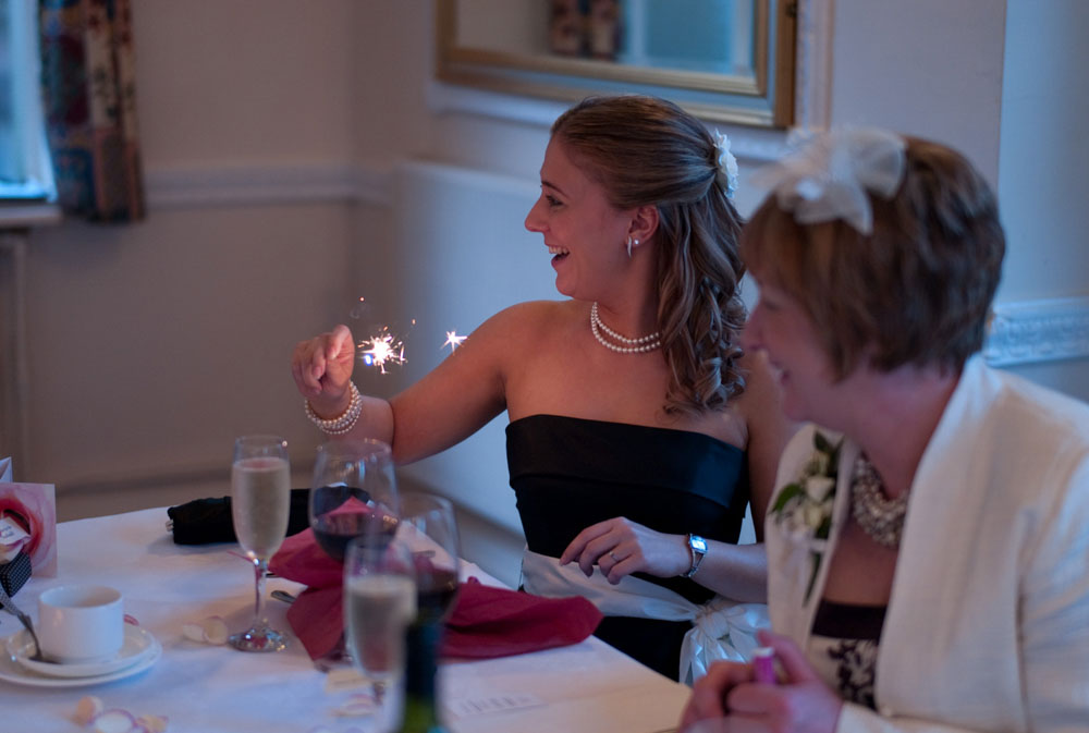Dani’s sister, the bridesmaid, waves her sparkler from her seat at the top table.