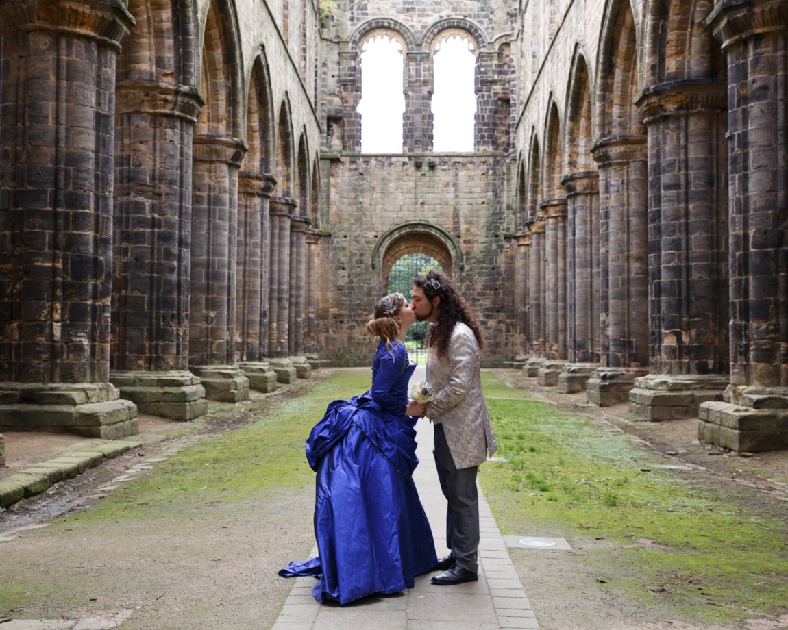 084 the couple kiss on the church pathway framed by the columns and arches kirkstall abbey wedding linsey and chris