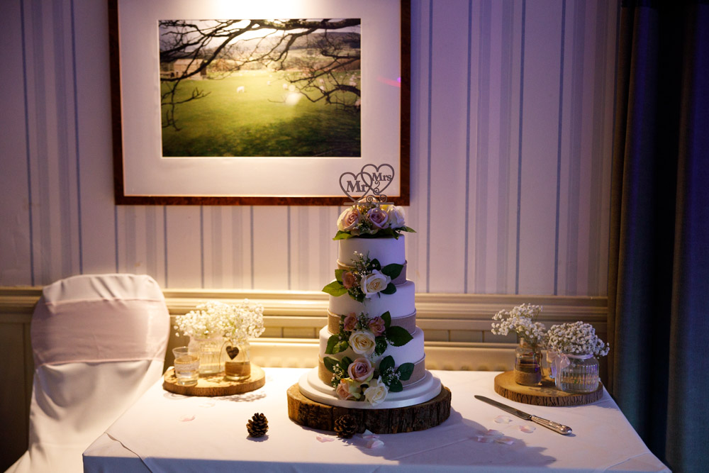 The wedding cake lit softly by a single wall lamp inside the evening reception room at Chevin Country Park Hotel.