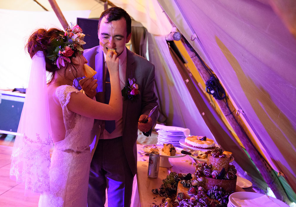 Bride and groom share a taste of their wedding cheesecake and smile.