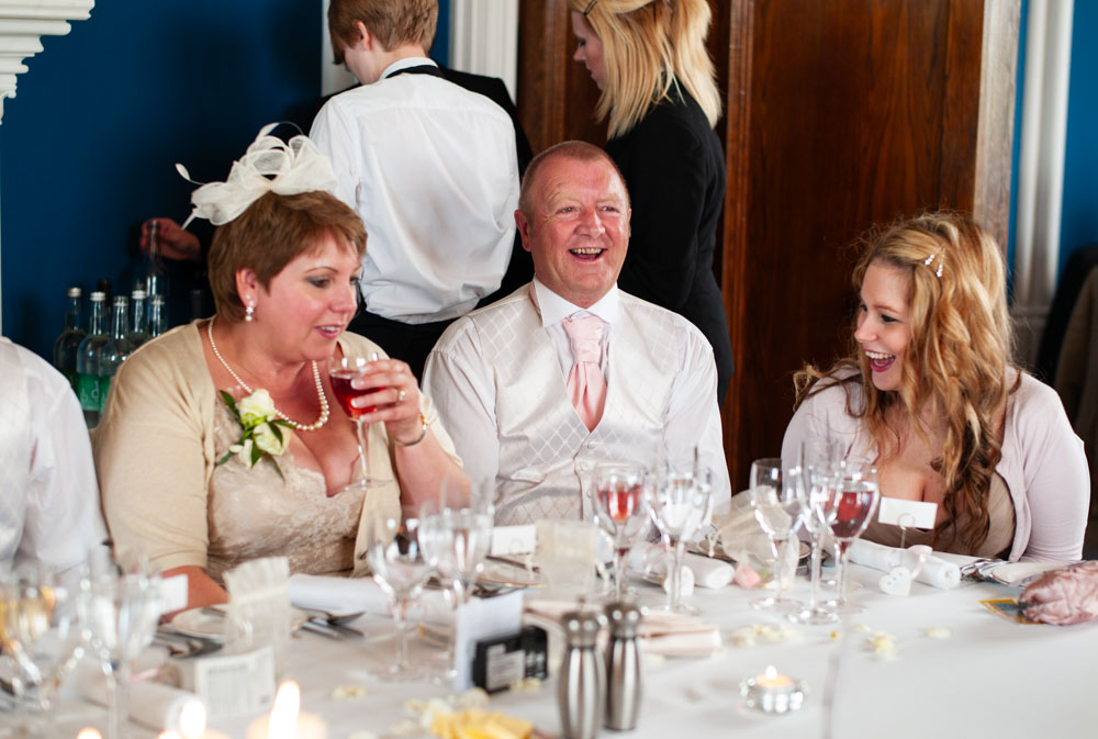 Groom’s parents and sister laughing together in the blue-walled wedding breakfast room at Allerton Castle