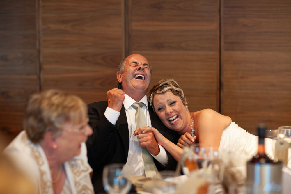 Sam leans into her father as he laughs and fist-pumps in amusement.