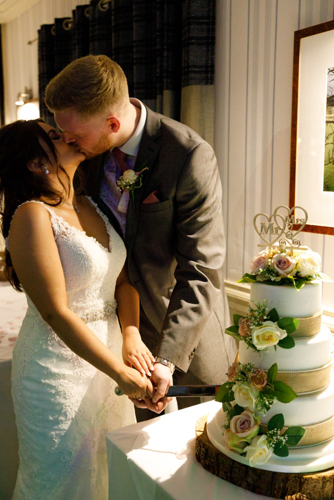 A soft kiss between Kyra and Matt just after cutting the cake, surrounded by guests.