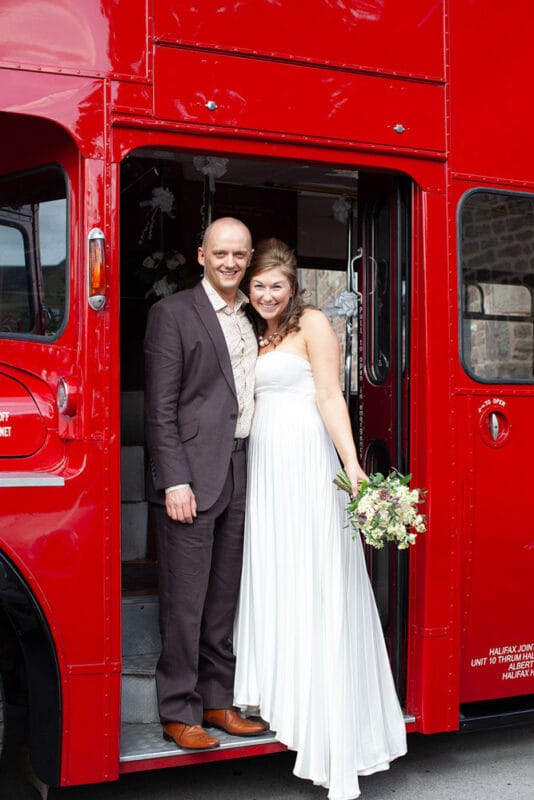 Happy couple smiling on the steps of their red wedding bus in Sheffield