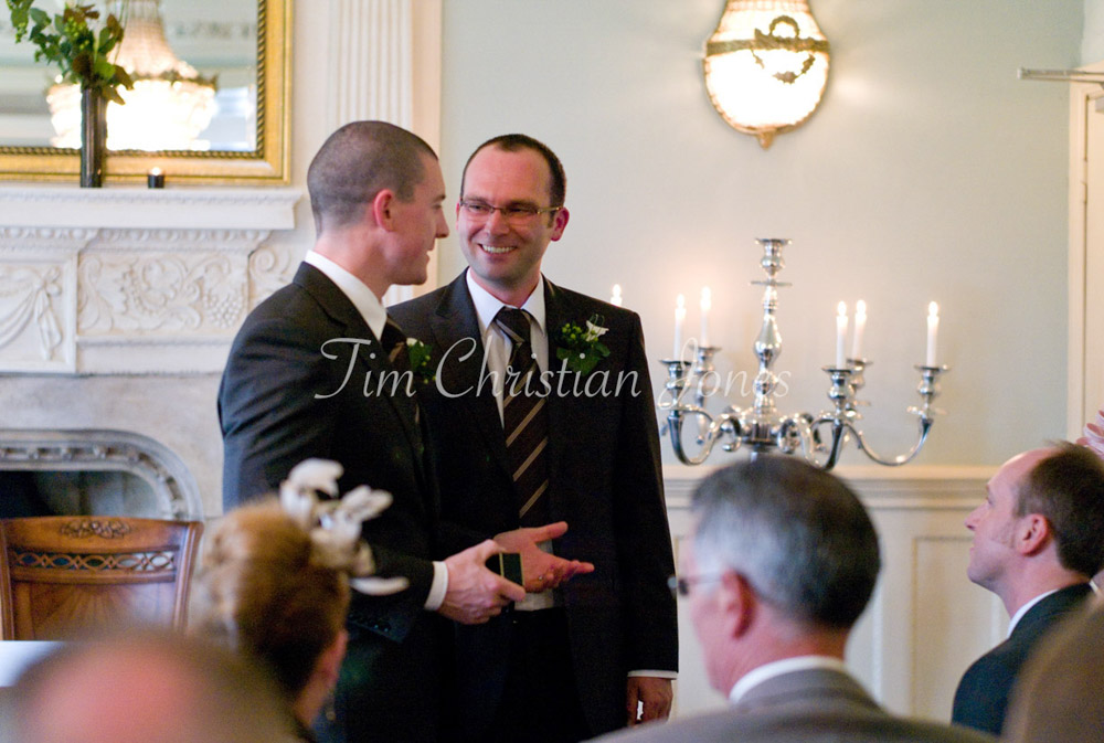 Groom and best man stand side by side, the ring box clasped with focus and care.