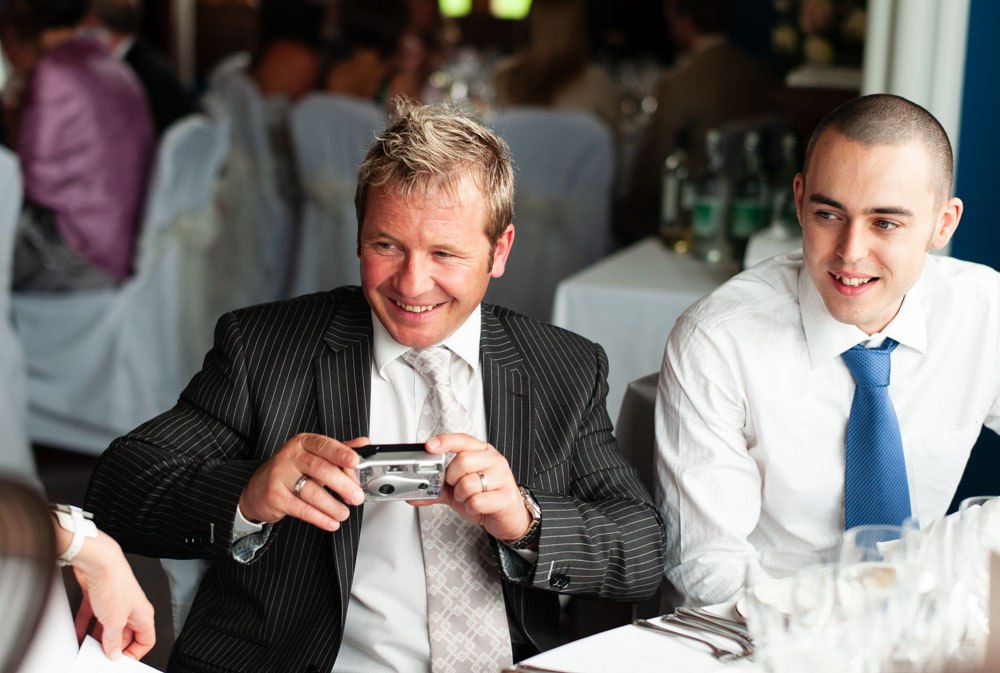 Guest holding a camera at the table, light falling gently across faces
