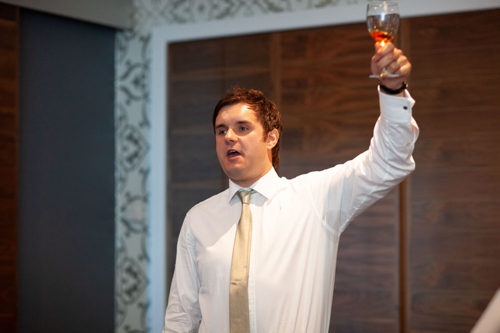 Best man #2 raises his glass with a big smile, toasting the happy couple at the end of the speeches.