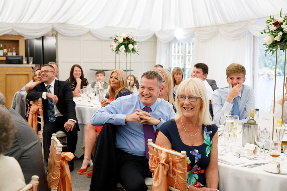 Wedding guests smiling as they listen to the speech.