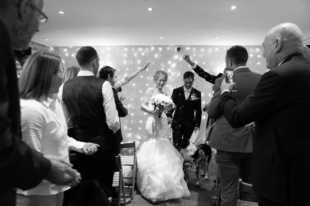 Bride laughs and dodges confetti in a playful black-and-white frame.