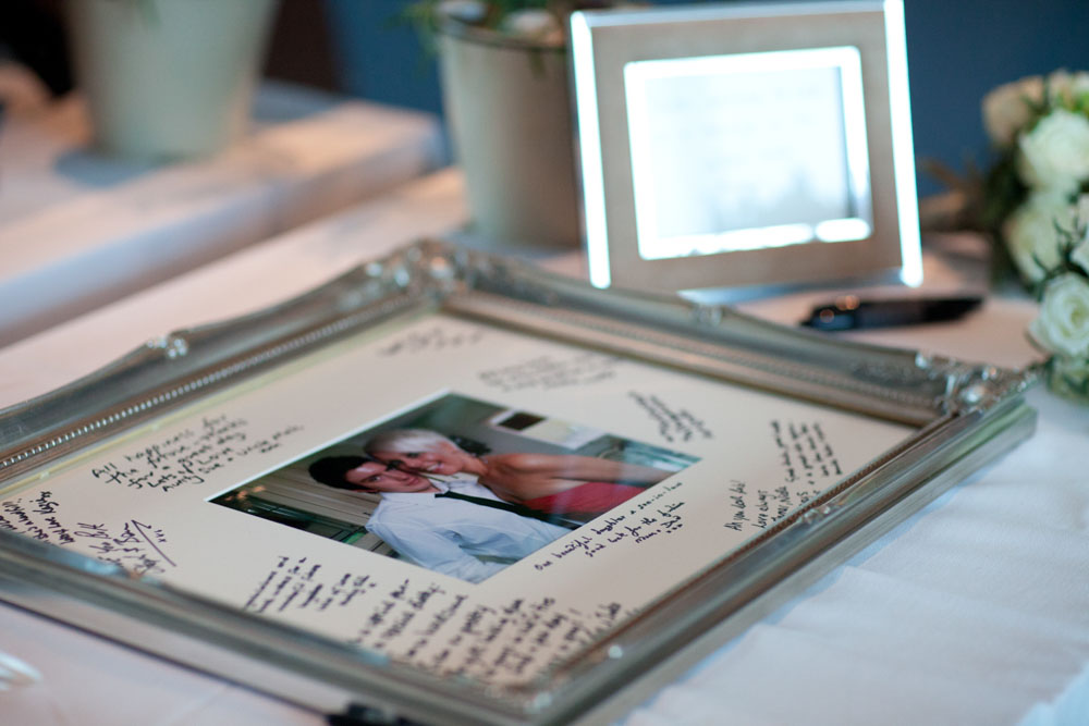 Sam & Tim pose with their custom wedding signature frame, surrounded by messages from guests.