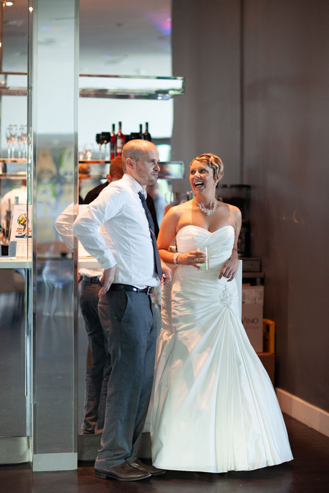 Sam stands chatting by the bar with a guest, both smiling naturally.