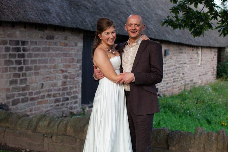 Wedding couple standing outside a beautiful barn at golden hour, relaxed and smiling
