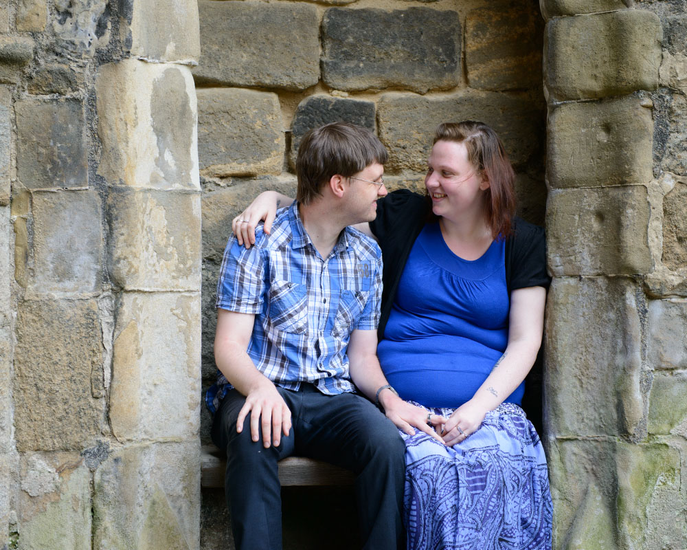 Rachel and Robert sitting together in an old stone arch, gazing at one another.