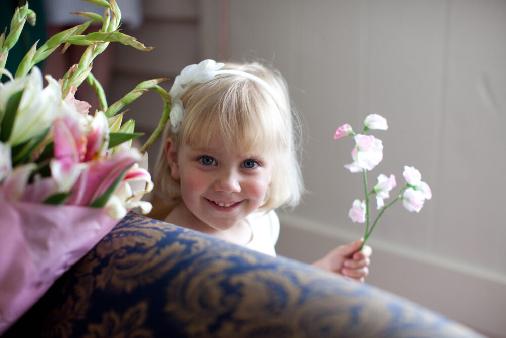 Little flower girl peeps from behind the sofa in the cottage used as the bridal suite