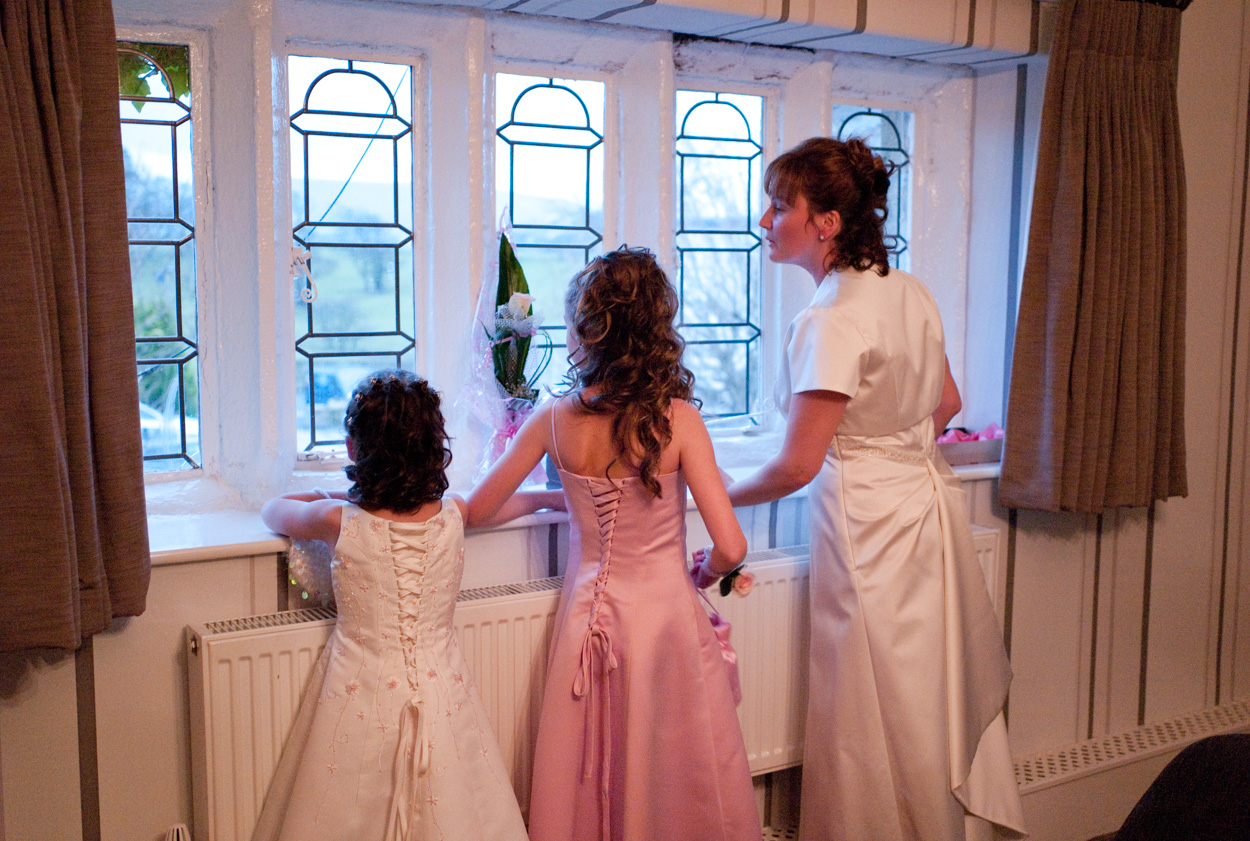 Bride and daughters looking through the leaded window at guests arriving