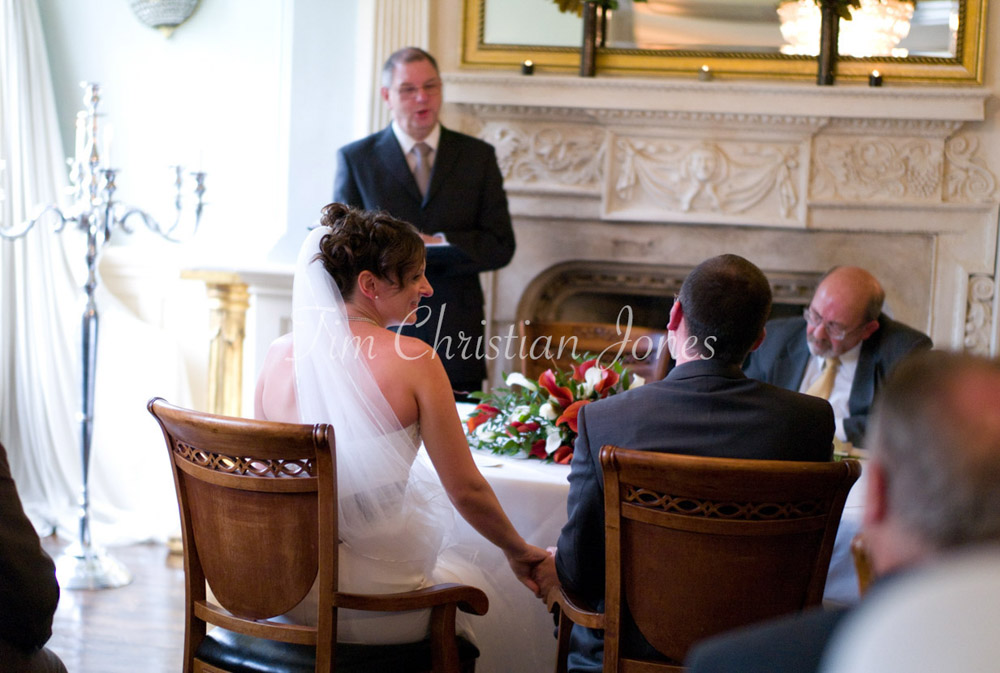 During the ceremony, the bride gently reaches to touch the groom’s hand as the registrar speaks.