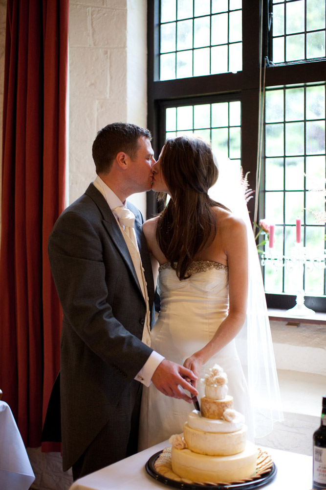 Lowri and Tim kiss while cutting their cheese wedding cake