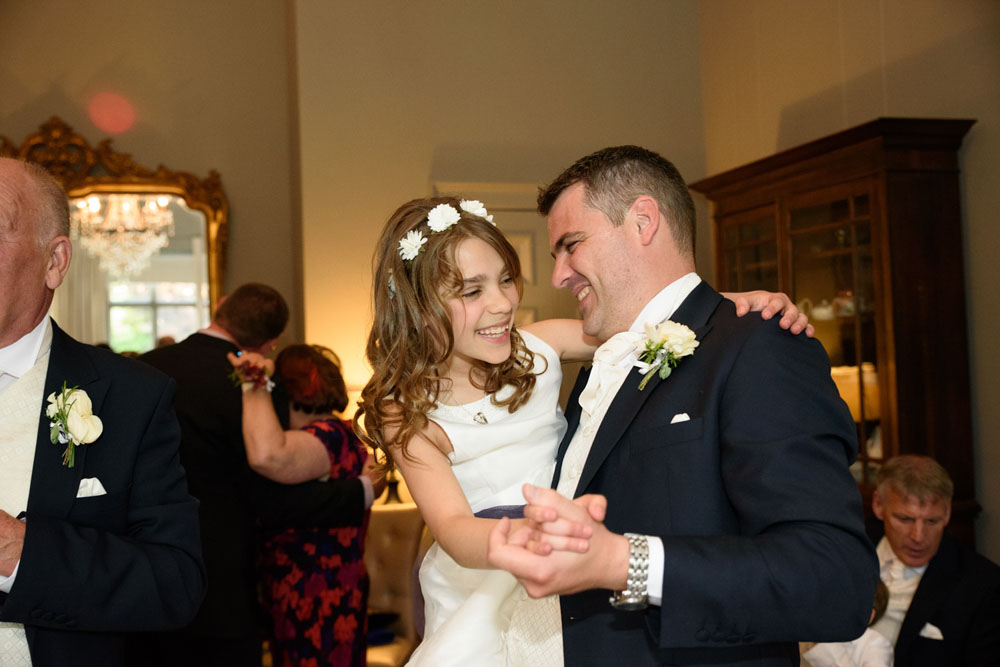 Groom and young bridesmaid dance happily together.